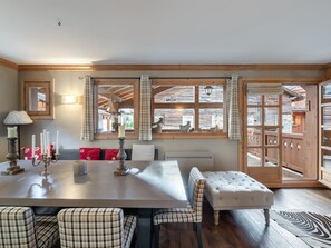 Ein Essbereich mit einem Holztisch, karierten Stühlen, einer Bank und Blick nach draußen durch große Fenster.