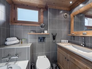 Ein modernes Badezimmer mit grauen Fliesen, einem Holzwaschtisch, einer weißen Toilette und einem Fenster über dem Waschbecken.