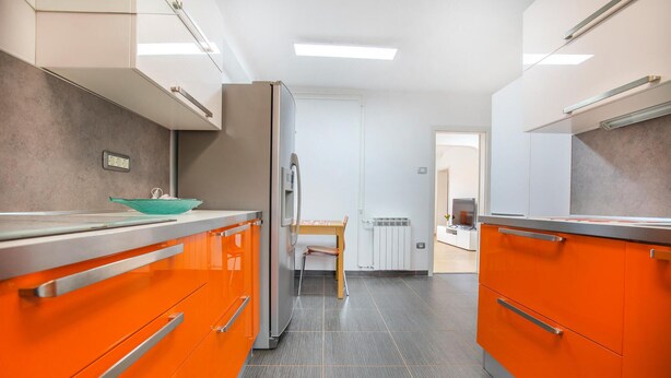A modern kitchen with orange cabinets, a stainless steel refrigerator, and a dining area with a table and chairs. - 3 bedroom cozy apartment in Koper (Koper)
