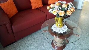 Un divano rosso con cuscini arancioni, un tavolino da caffè in vetro con base intrecciata e un vaso con fiori.
