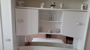 Una camera da letto con un letto caratterizzato da biancheria floreale, un armadio bianco con ante aperte e uno scaffale con oggetti decorativi.