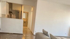 A spacious living area with a large grey sofa and a wooden coffee table. A kitchen with modern appliances is visible in the background. - Charming Renovating Mets Apartment Athina (Athens)