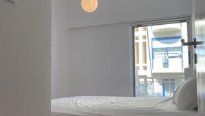 A bedroom with a bed, a hanging light fixture, and a window with a view of buildings. - Charming Renovating Mets Apartment Athina (Athens)
