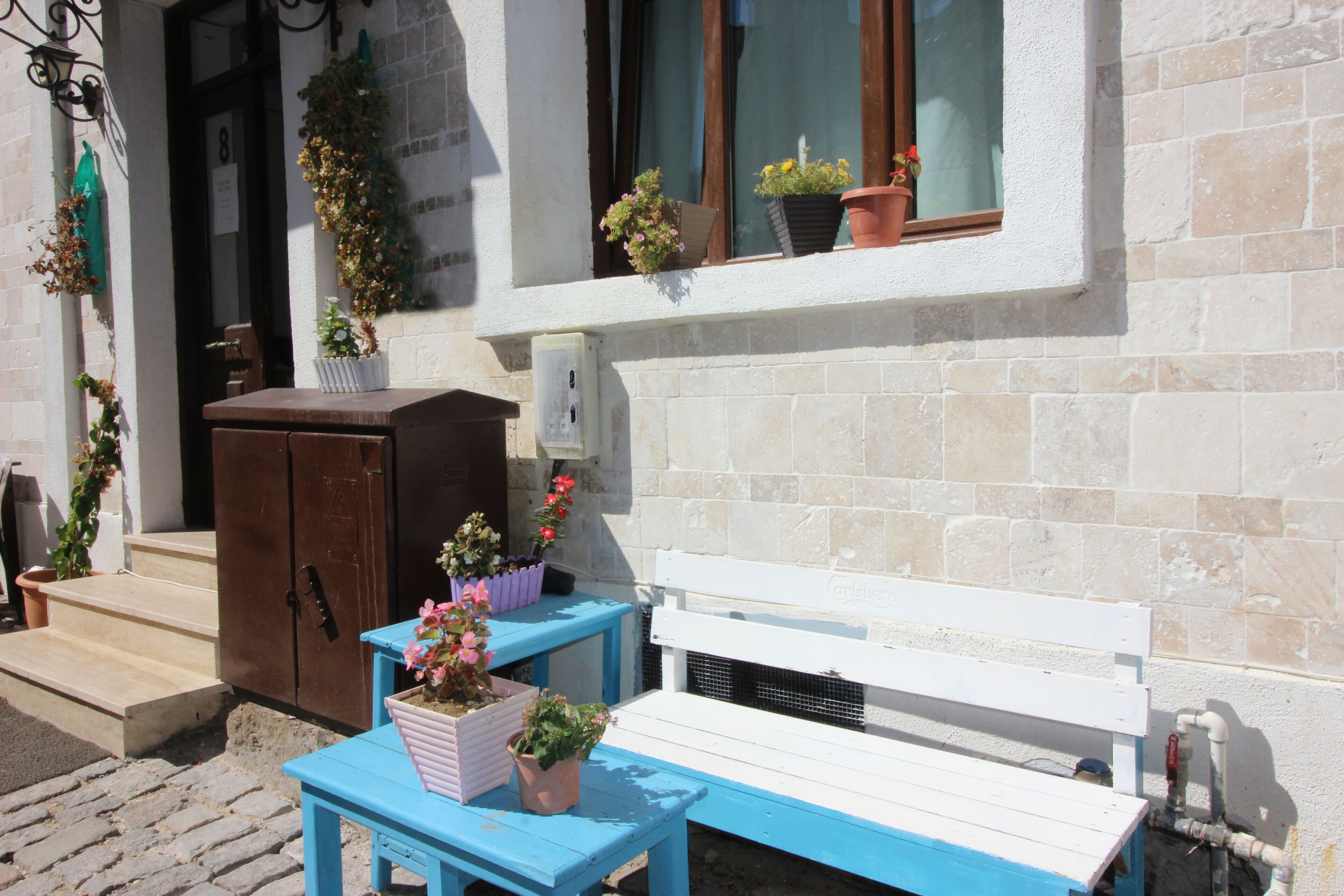 A blue bench and table outside a building with potted plants on the windowsill.