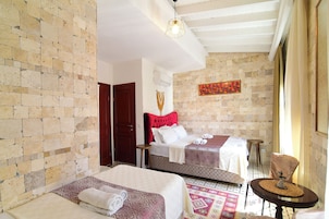 Habitación de hotel con dos camas, cabecera roja, alfombra estampada y una pequeña mesa redonda con un objeto decorativo.
