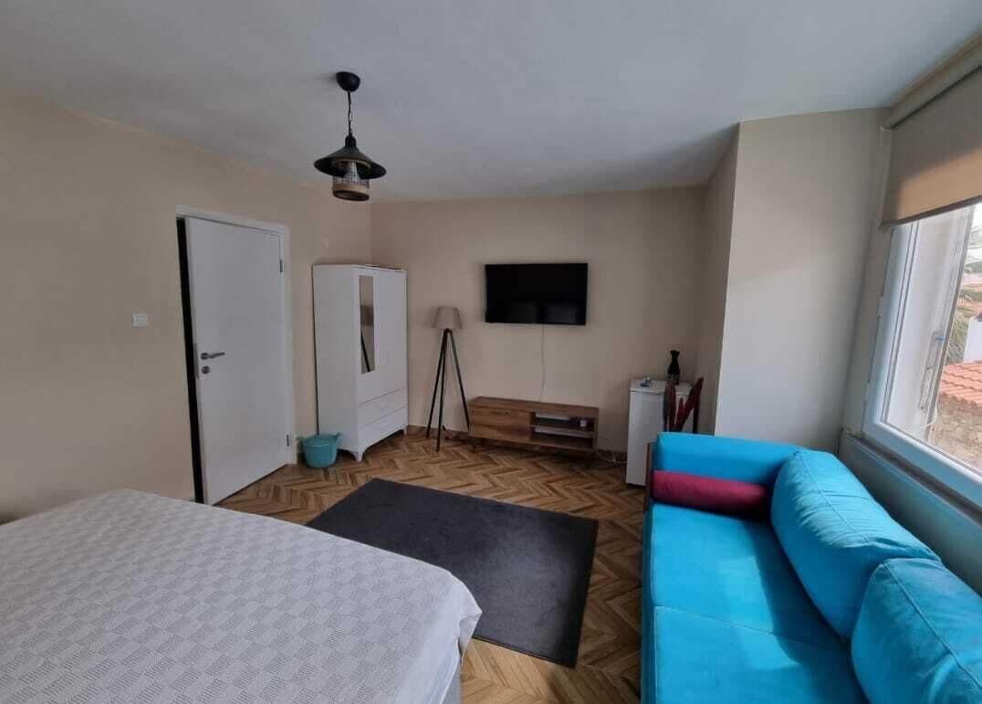 Una habitación con cama, sofá azul, televisión, armario y ventana.