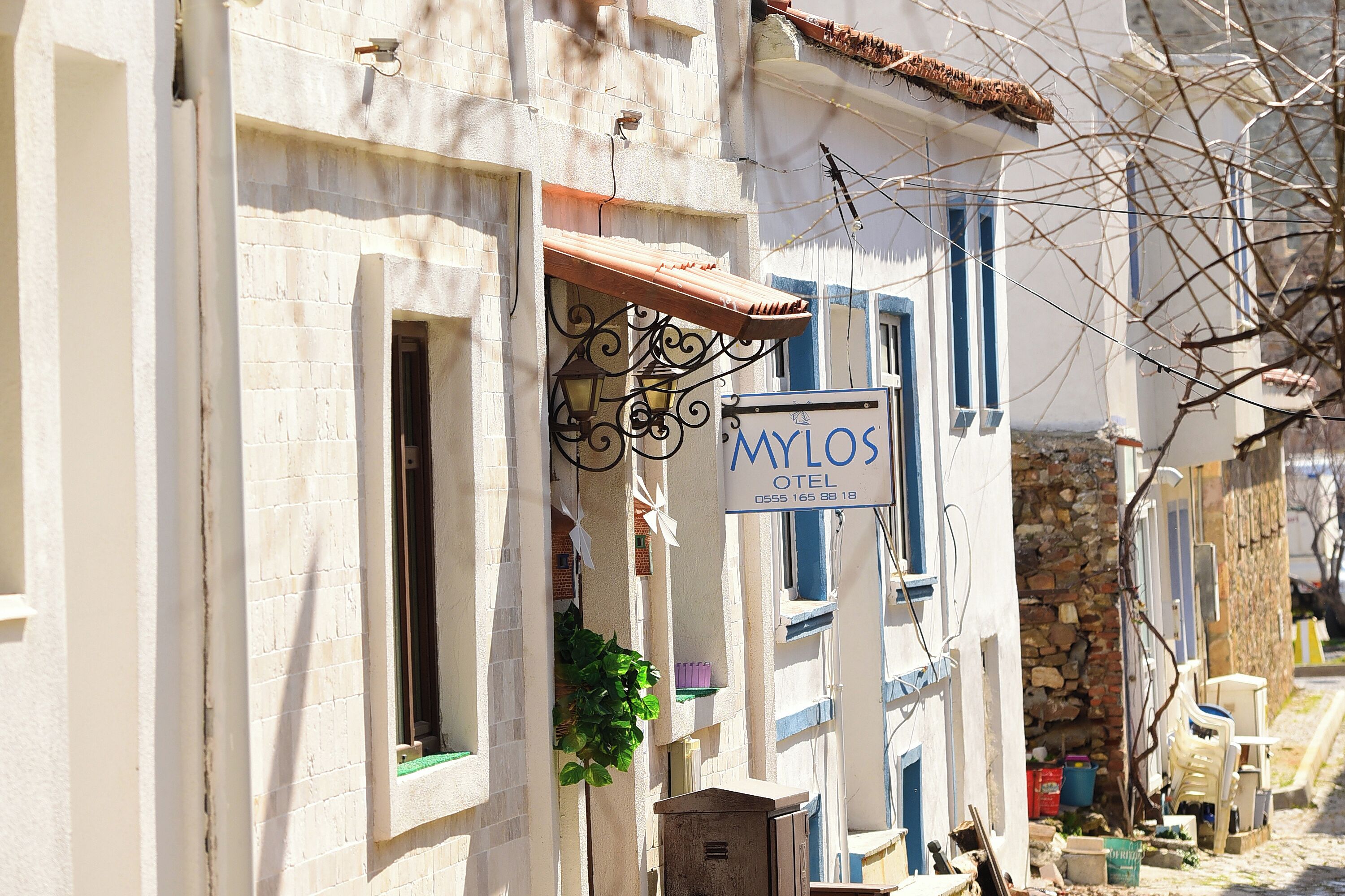 A hotel named "MYLOS" with a signboard, a stone wall, and a narrow street.