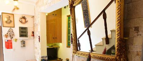 A room with a tiled floor, a wooden table, a chair, a mirror with an ornate frame, and a decorative vase.