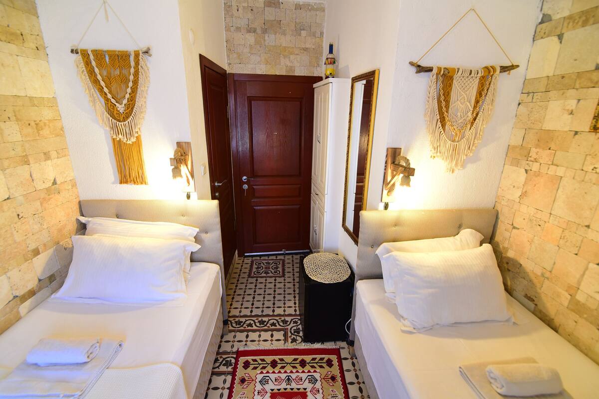 Una habitación de hotel con dos camas, una pequeña zona de estar, una puerta y adornos de macramé en las paredes.
