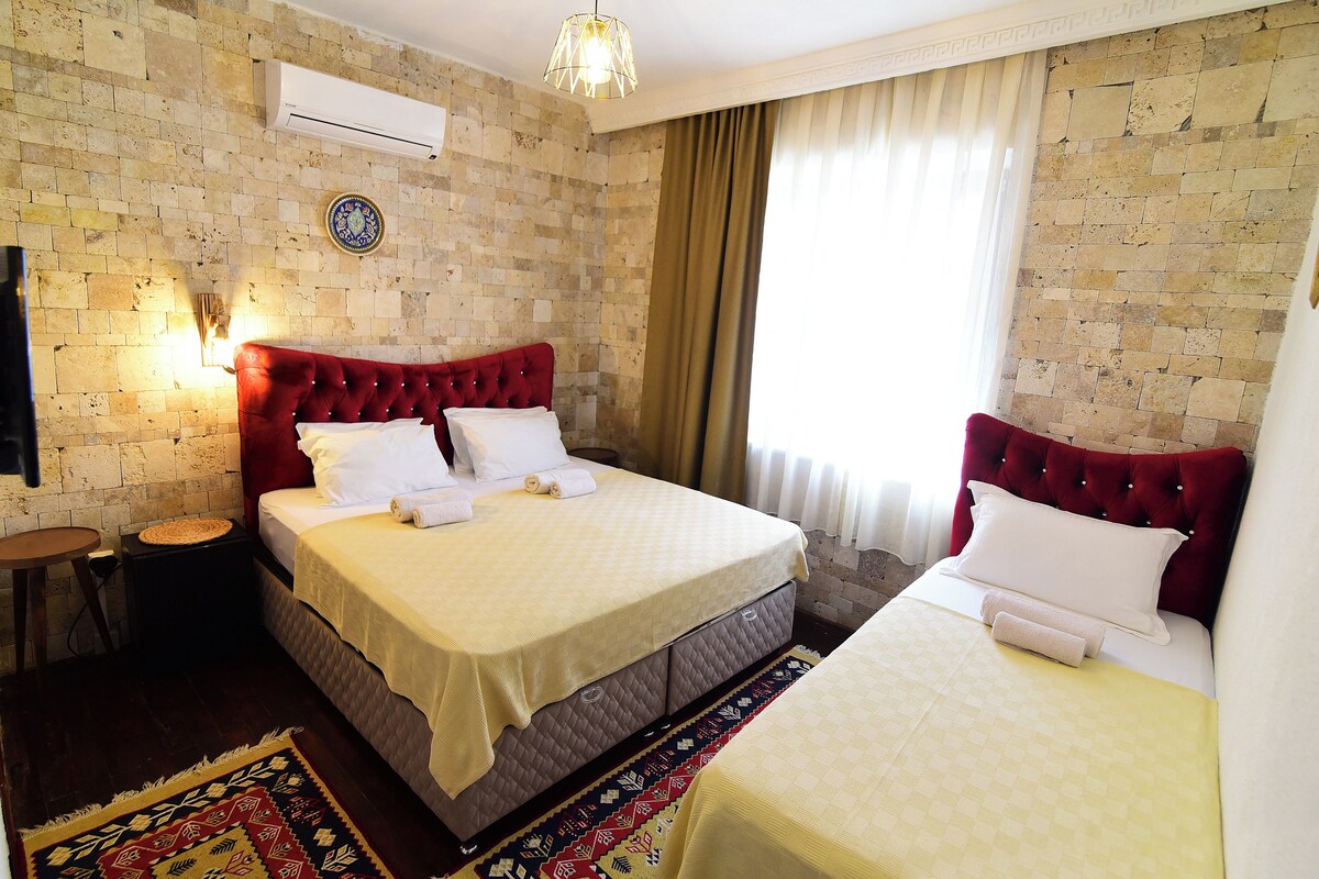 Habitación de hotel con una cama grande, una cama más pequeña, un cabecero rojo, aire acondicionado instalado en la pared y una alfombra estampada.