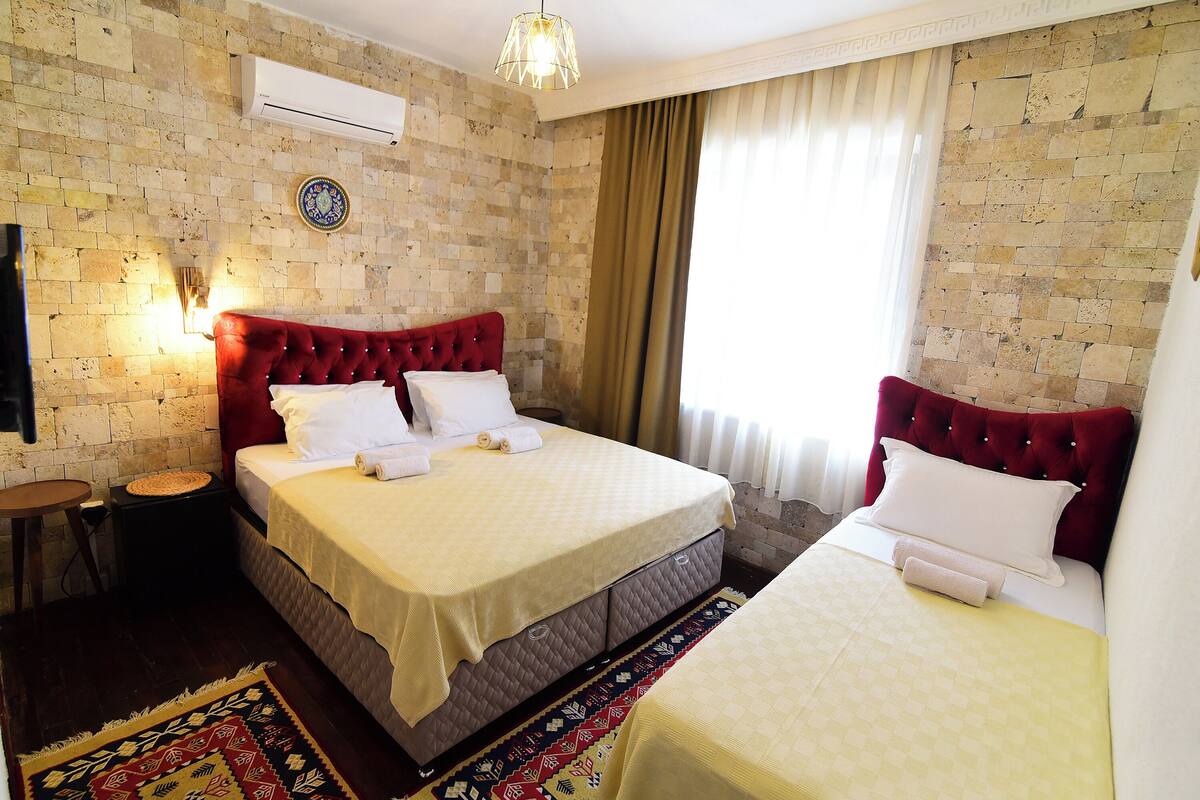 Habitación de hotel con una cama grande, una cama más pequeña, un cabecero rojo, aire acondicionado instalado en la pared y una alfombra estampada.