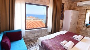 A hotel room with a large window, a bed with towels, a wardrobe, and a blue sofa. - Mylos Otel (Bozcaada)