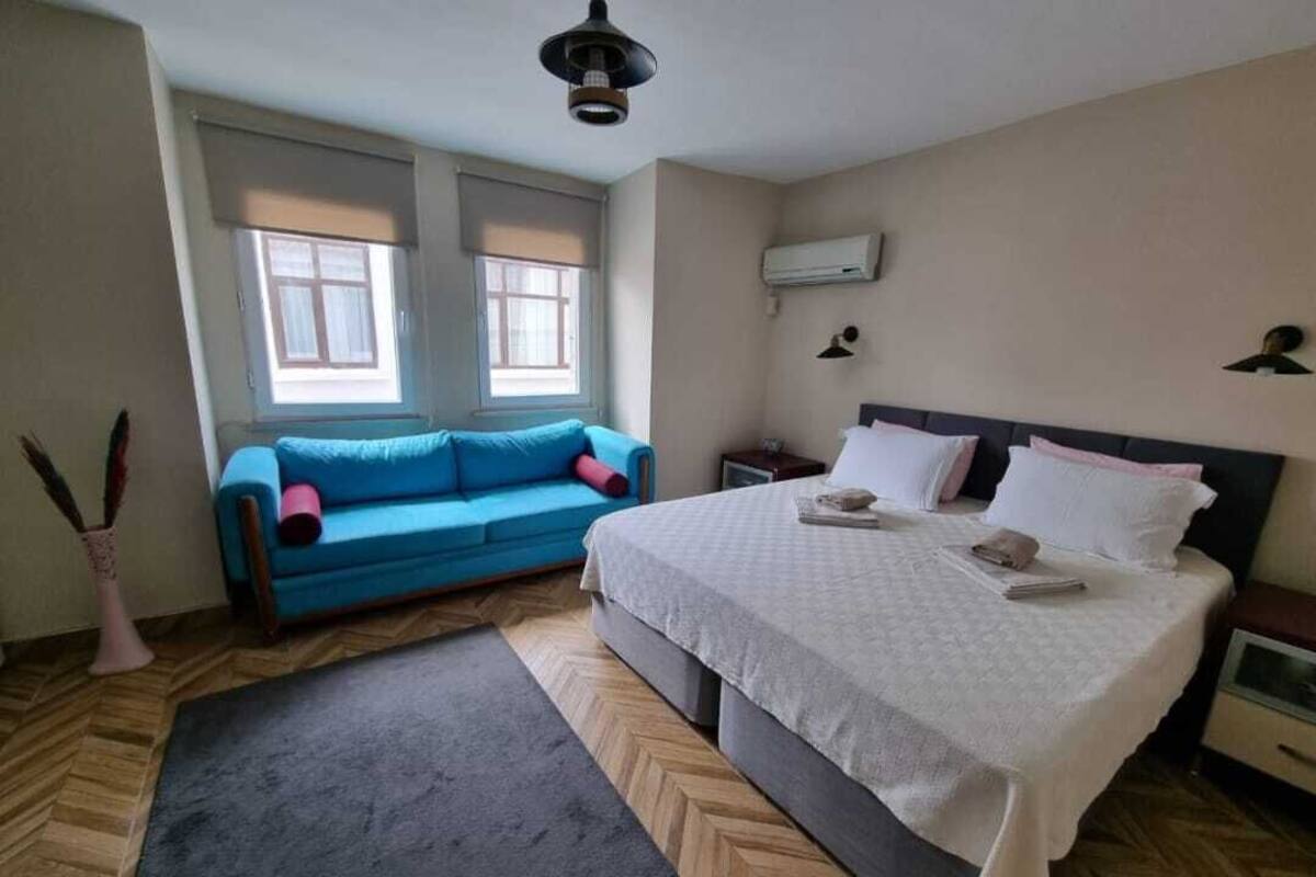 Un dormitorio con cama, un sofá azul, una ventana y un aire acondicionado de pared.