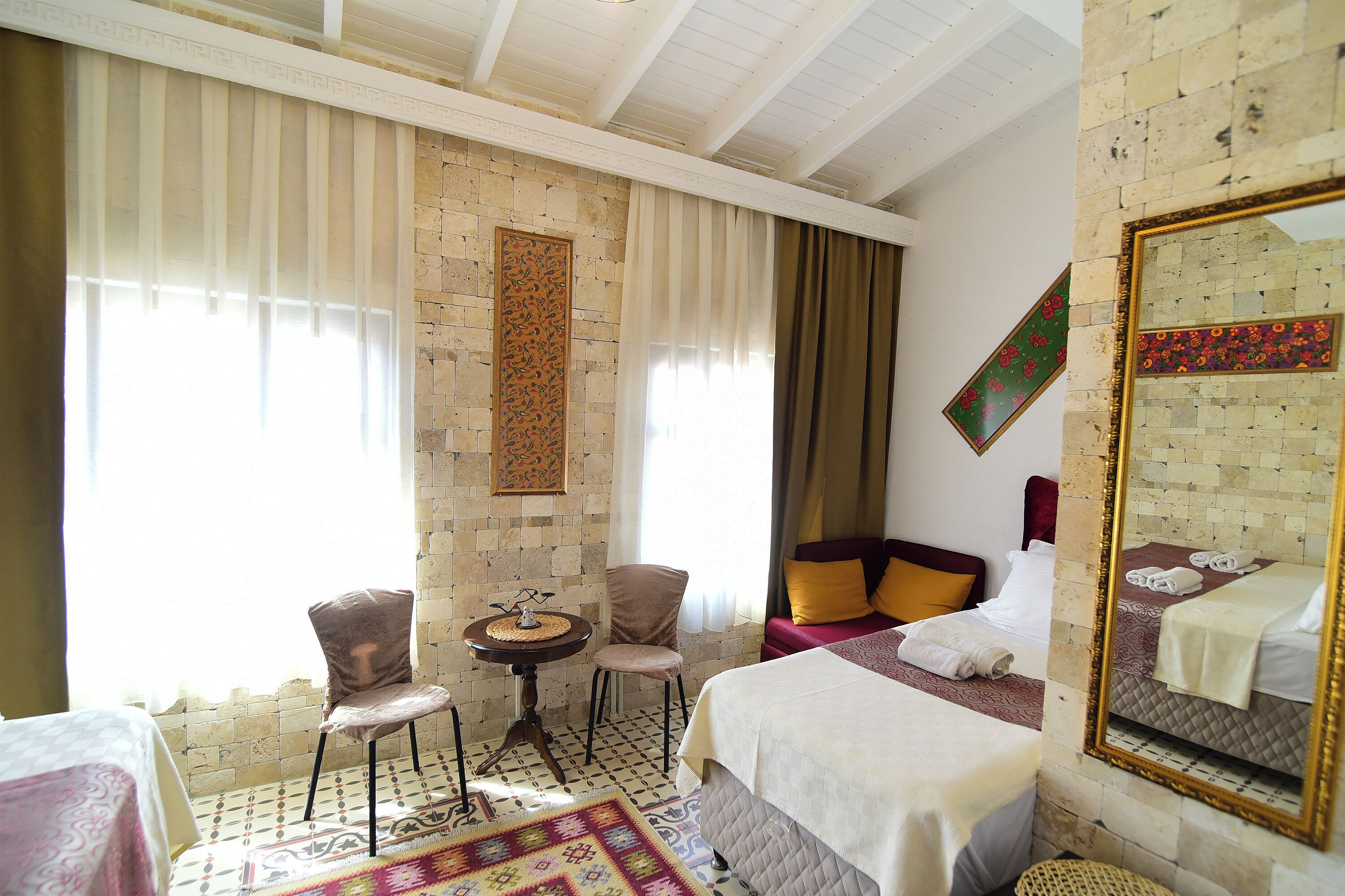 Une chambre d’hôtel avec un lit, deux chaises, une petite table et un grand miroir.