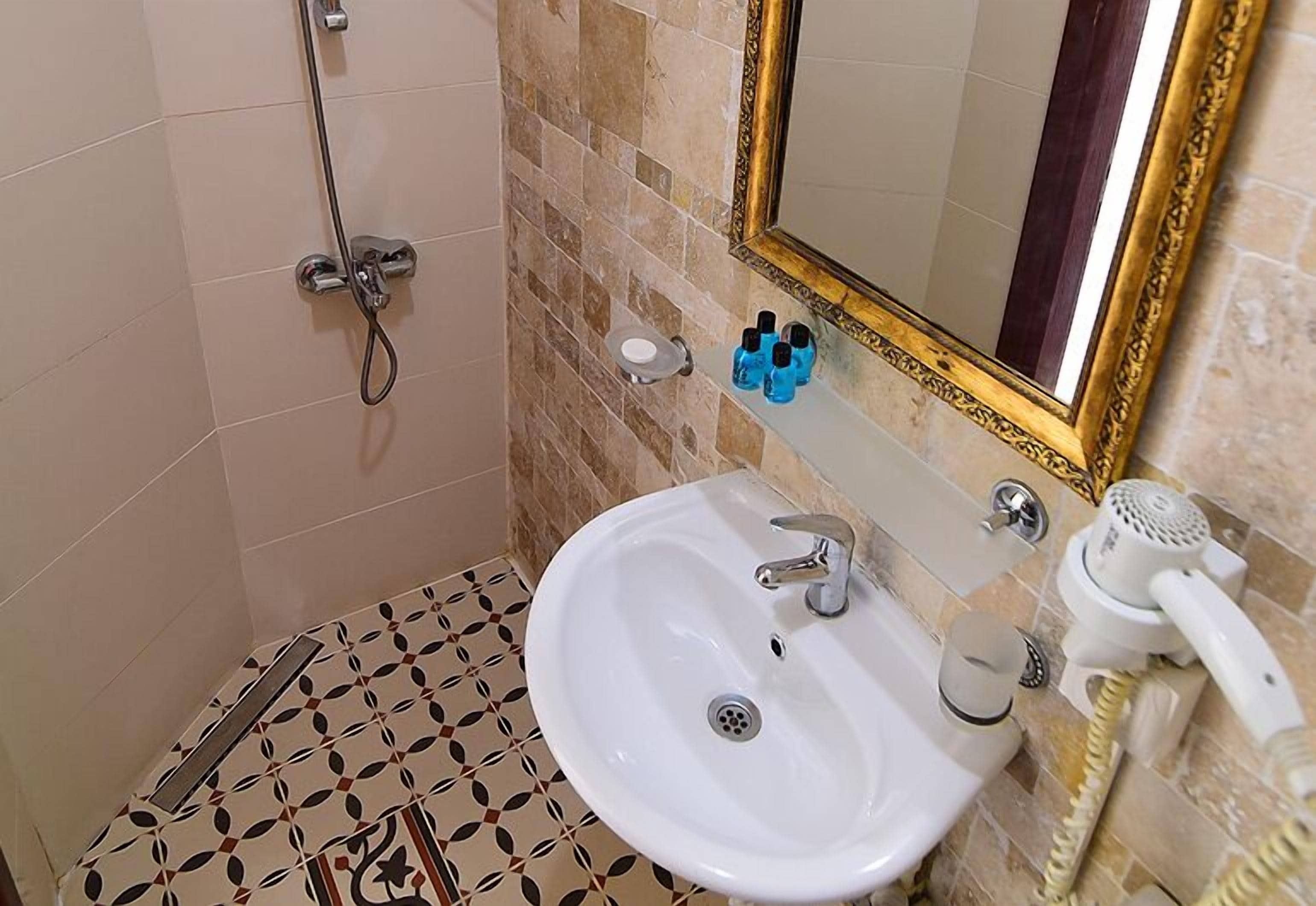 A bathroom with a white sink, a mirror with a gold frame, and a shower.