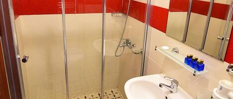 Une douche avec une porte en verre, un lavabo avec un miroir et un mur recouvert de carreaux rouges et blancs.