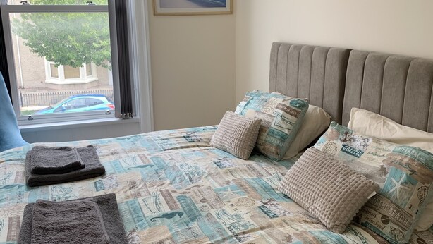 A bedroom with a bed featuring a coastal-themed bedspread, a headboard, and several pillows. - First floor, recently renovated central Llandudno apartment (Llandudno)