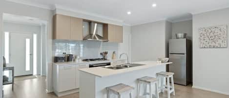 A modern kitchen with white cabinetry, a central island with stools, a stainless steel range hood, and a refrigerator.