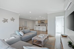 Ein modernes Wohnzimmer mit einem grauen Sofa, einem Couchtisch und einer Küche im Hintergrund.