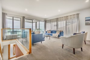 A spacious living room with a blue sofa, a white armchair, and a glass railing overlooking a balcony. - Vue Sur La Mer by Ready Set Stay - View of the sea (Mount Martha)