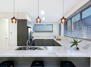 A modern kitchen with a marble countertop, stainless steel appliances, and pendant lighting. - Vue Sur La Mer by Ready Set Stay - View of the sea (Mount Martha)