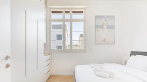 A minimalist bedroom with a bed, a window, and a painting on the wall. - An amazing gem in the heart of TelAviv (Tel Aviv)
