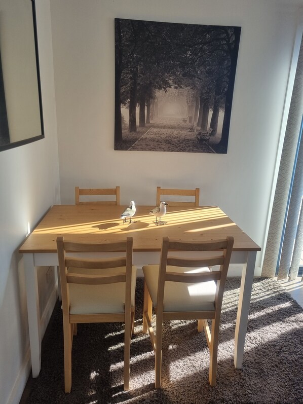 Une table à manger avec quatre chaises, un tableau encadré au mur et une vue sur l’extérieur.