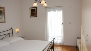 A bedroom with a single bed, a window with curtains, a wall-mounted picture, and a wall-mounted light fixture. - Beautiful Apartment With Sea View, Trogir, Croatia (Trogir)