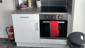 Una cocina compacta con armarios blancos, una estufa negra y un guante de horno rojo.