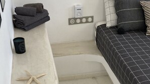 Een kleine slaapkamer met een bed, een klein nachtkastje, een wandlamp en een nachttafeltje.