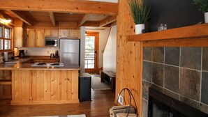 Una cucina in stile rustico con arredamento in legno, un'isola centrale, un camino in pietra e vista sull'esterno tramite una porta.