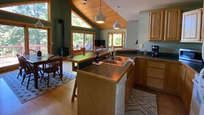 A spacious kitchen with wooden cabinets, a dining area with a table and chairs, and large windows allowing natural light. - Carriage House - Chequamegon Bay, Bayfield (Bayfield)