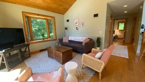 A spacious living room with a large window, a television, a sofa, and a coffee table. - Carriage House - Chequamegon Bay, Bayfield (Bayfield)