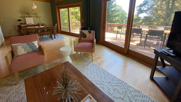 A spacious living room with a wooden ceiling, large windows, a dining area, and a television. - Carriage House - Chequamegon Bay, Bayfield (Bayfield)