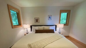 A large bed with a headboard, two bedside lamps, and a window on each side. - Carriage House - Chequamegon Bay, Bayfield (Bayfield)