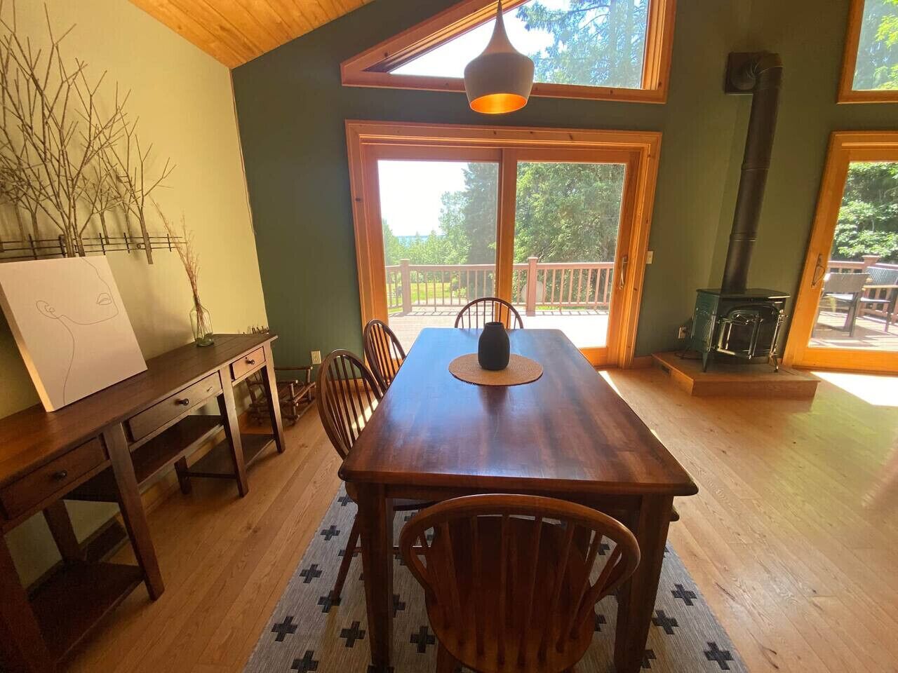 A dining area with a wooden table and chairs, a large window with a view of the outdoors, and a fireplace.