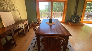 A dining area with a wooden table and chairs, a large window with a view of the outdoors, and a fireplace. - Carriage House - Chequamegon Bay, Bayfield (Bayfield)