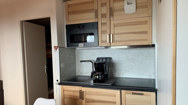 Una cocina compacta con armarios de madera, microondas, cafetera y un ventanal pequeño.