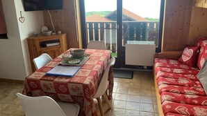 Una habitación acogedora con una mesa de comedor para dos, un sofá, un televisor y vistas a un edificio de tejas rojas.