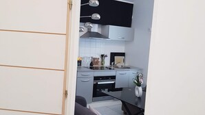 Cozinha compacta com eletrodomésticos modernos, espaço de refeições com sofá cinza e porta branca que dá acesso a outro ambiente.