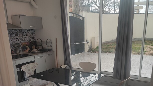 Cozinha moderna com área de jantar, sofá e vista através de uma porta de vidro.