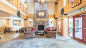 A spacious lobby with a stone fireplace, wooden walls, and a high ceiling. There are two sofas and a coffee table in the center. - Right next to Super Bee Lift, wifi, underground parking (Copper Mountain)