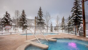 A pool area with a hot tub, surrounded by snow-covered trees and a mountainous backdrop. - Right next to Super Bee Lift, wifi, underground parking (Copper Mountain)