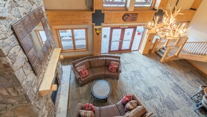 A spacious loft-style room with a stone wall, a large wooden ceiling, and a fireplace. There is a curved brown sofa with red pillows and a round coffee table in the center. - Right next to Super Bee Lift, wifi, underground parking (Copper Mountain)