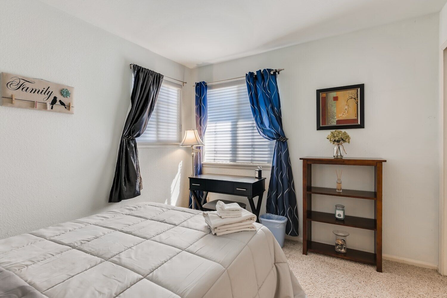Une chambre à coucher comprenant un lit, un bureau, une chaise, une lampe, une étagère avec des objets décoratifs et un panneau fixé au mur.