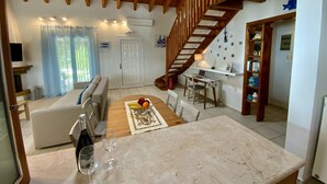Een ruime woonkamer met een houten trap, een eettafel met een laptop, en een keuken met een marmeren aanrechtblad.