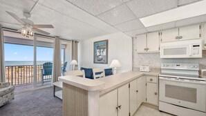 A kitchen with a view of the beach, a ceiling fan, and a microwave.