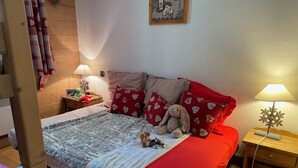 Een slaapkamer met een bed, kussens, een teddybeer, een lamp en een nachtkastje.