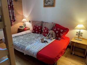Un dormitorio con una cama, almohadas, un osito de peluche, una lámpara y una mesita de noche.