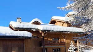 Een houten chalet met een stenen fundering, meerdere balkons en een sneeuwbedekt dak.